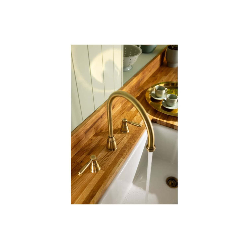 Shiny brass kitchen sink tap with flowing water, set on a wooden countertop in a modern kitchen design. Elegant fixtures complement the warm wood tone and contemporary decor.