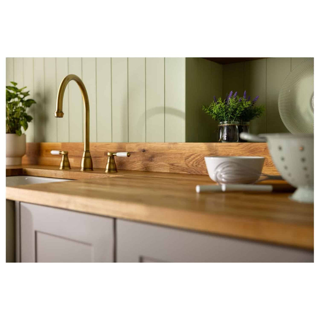 Shabby Chic Kitchen with wooden countertop, gold finish tap, and pastel green panelled wall, decorated with plants and ceramics for a cosy bathroom vibe.