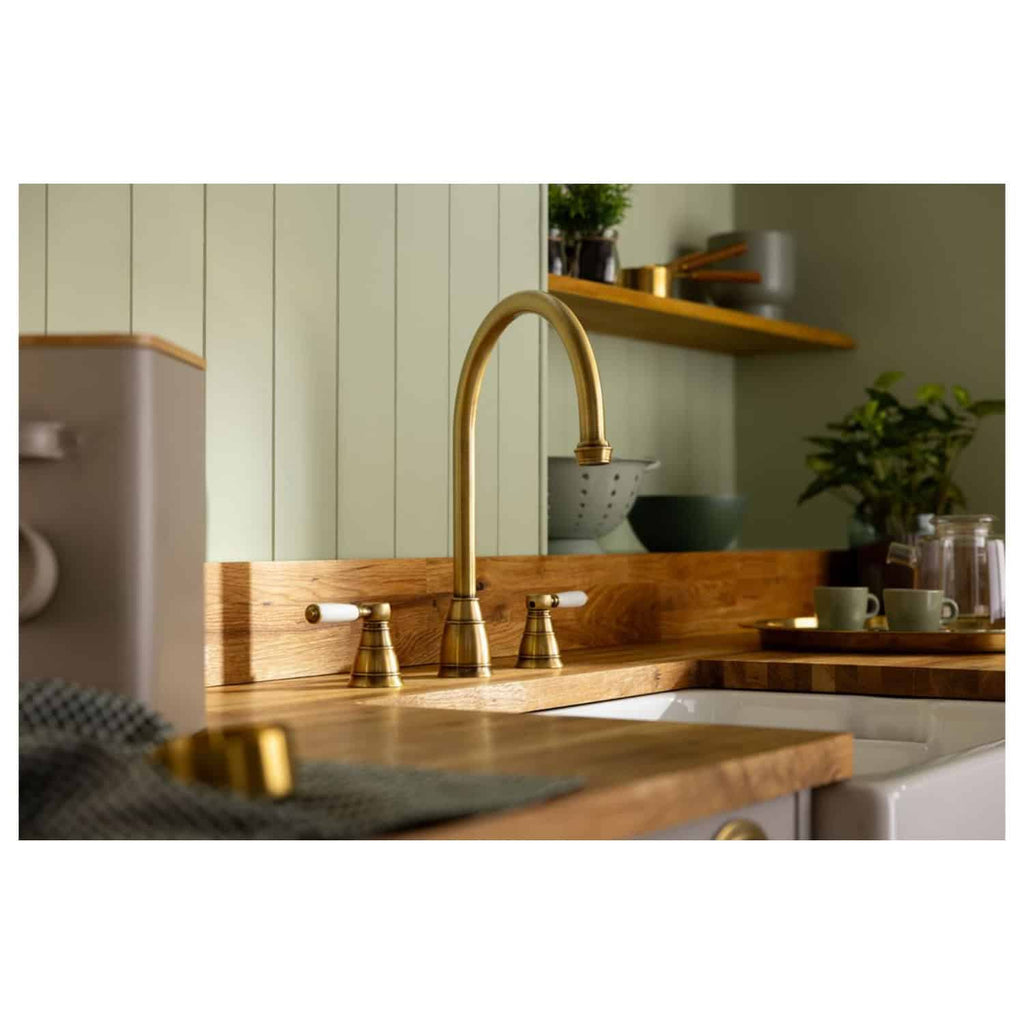 Polished gold kitchen tap with a vintage design, installed on a wooden countertop in a modern kitchen setting with light green panelled walls.