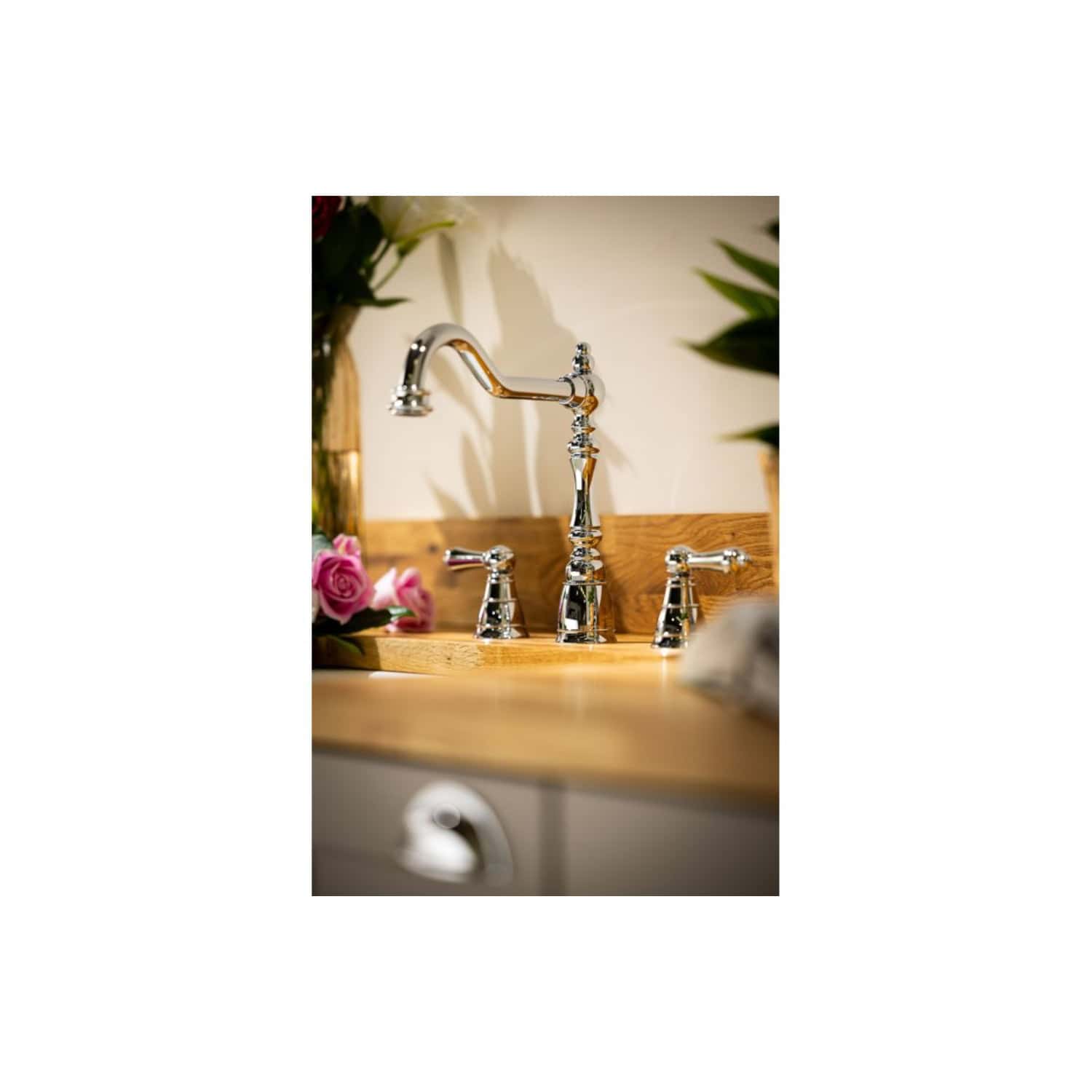 Shiny chrome kitchen sink tap with vintage design, flowers, and greenery in the background, close-up shot. Elegant bathroom fixtures for classic or rustic style kitchens.