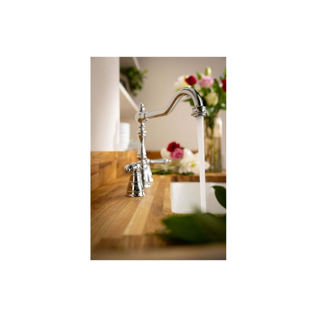 Shiny chrome kitchen faucet with running water, wooden countertop, and a blurred background featuring a vase of fresh colourful flowers, highlighting modern bathroom and kitchen fixtures.