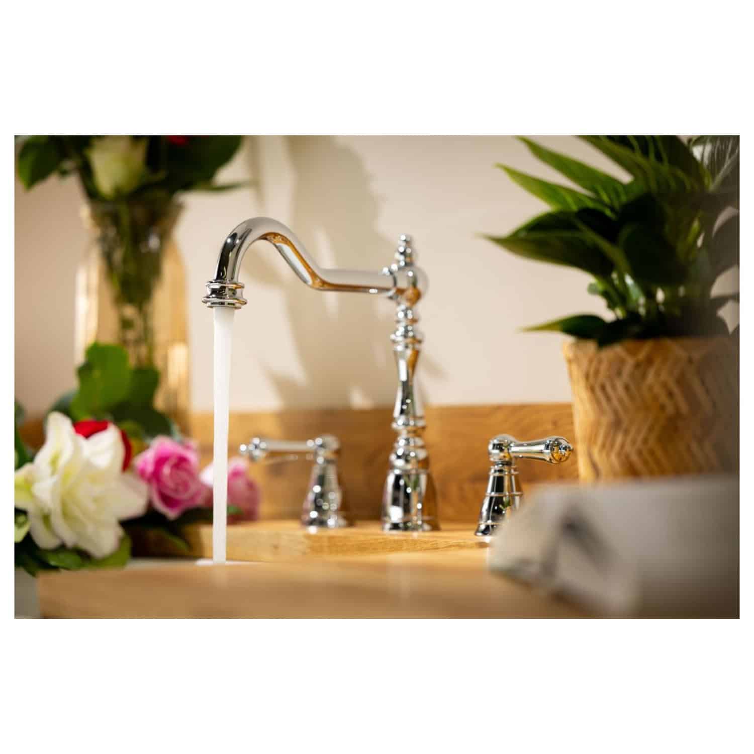 Shiny chrome bathroom tap with flowing water, surrounded by fresh flowers and potted plants, showcasing elegant and modern bathroom fixtures for a stylish interior.