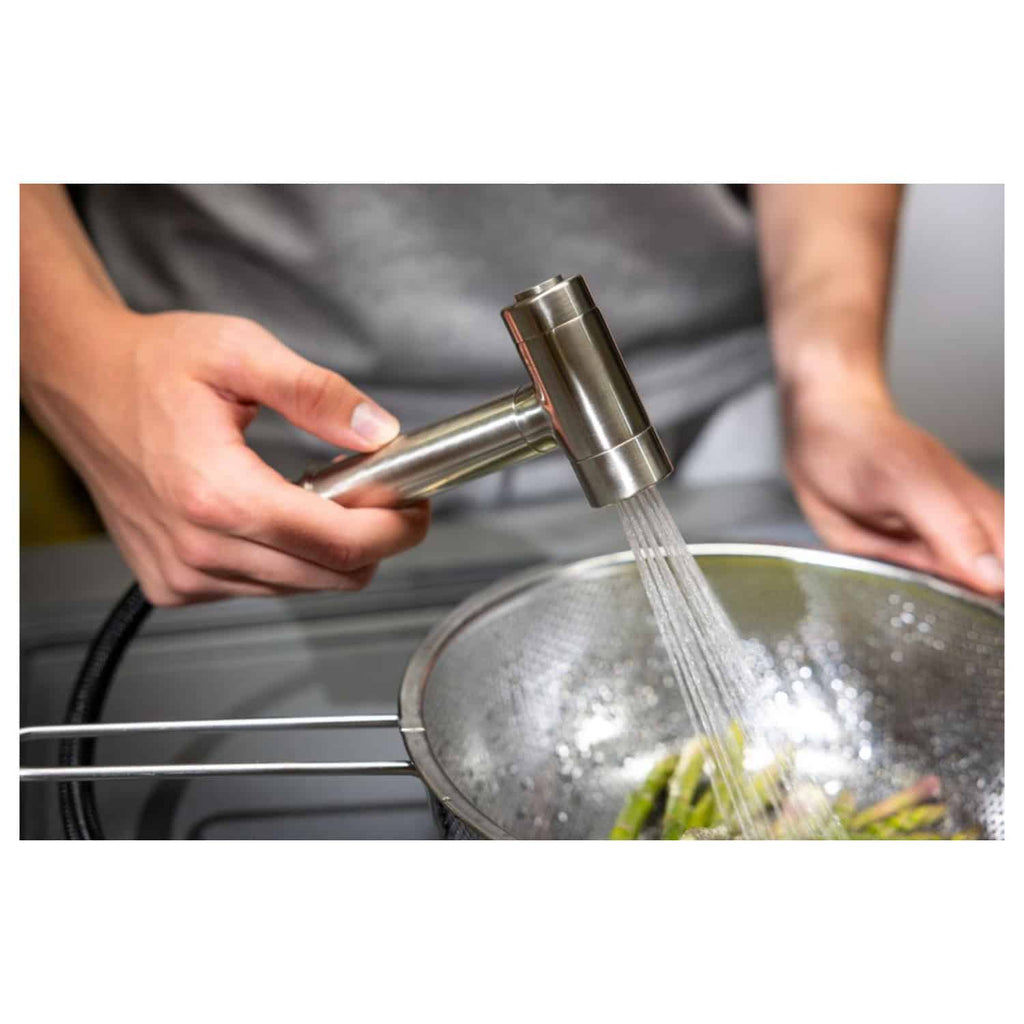 Faucet water filter system being used to rinse vegetables in a modern kitchen sink.