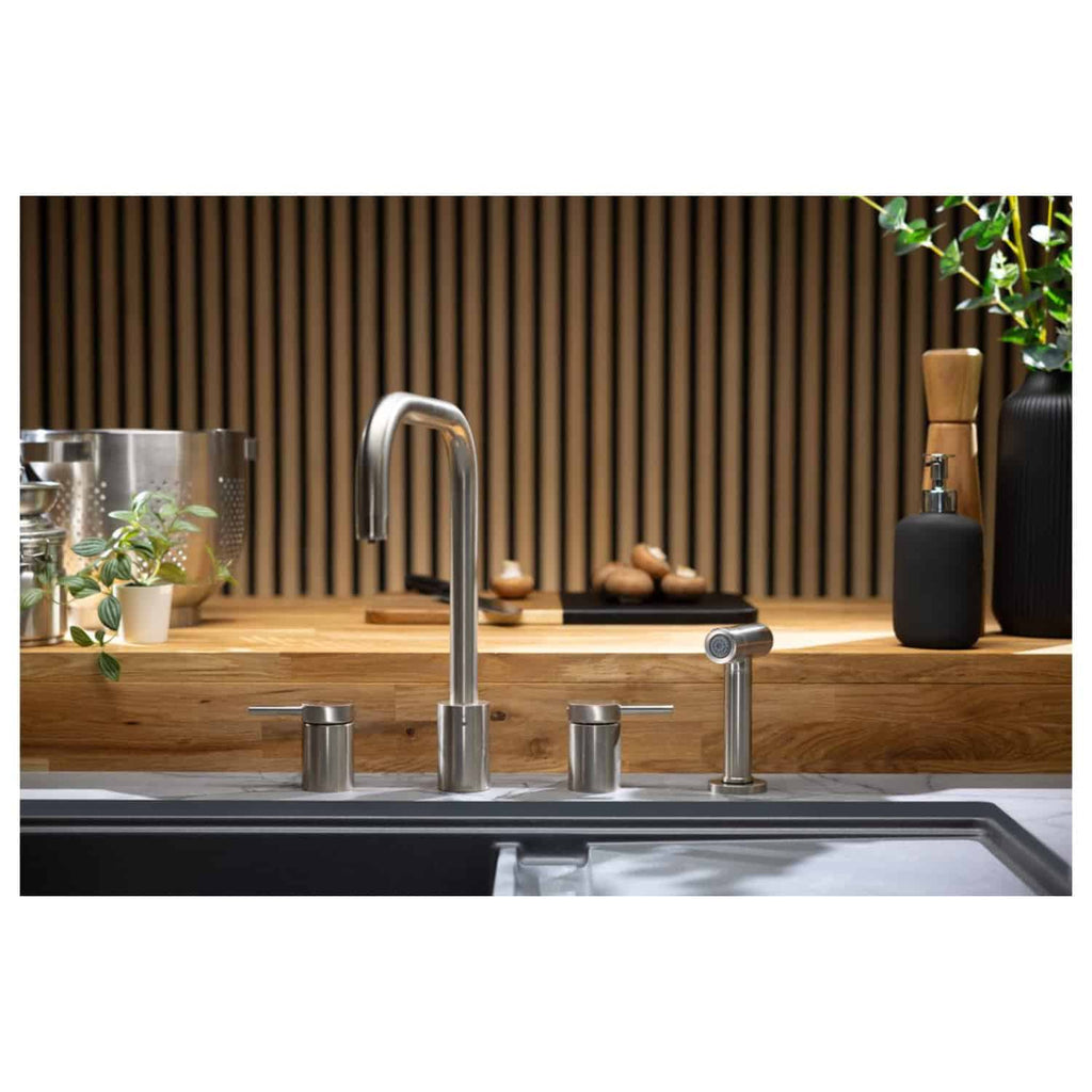 Sleek stainless steel kitchen faucet with modern design, surrounded by eco-friendly elements like potted plants, wooden accents, and black decor pieces, in a contemporary kitchen setting.