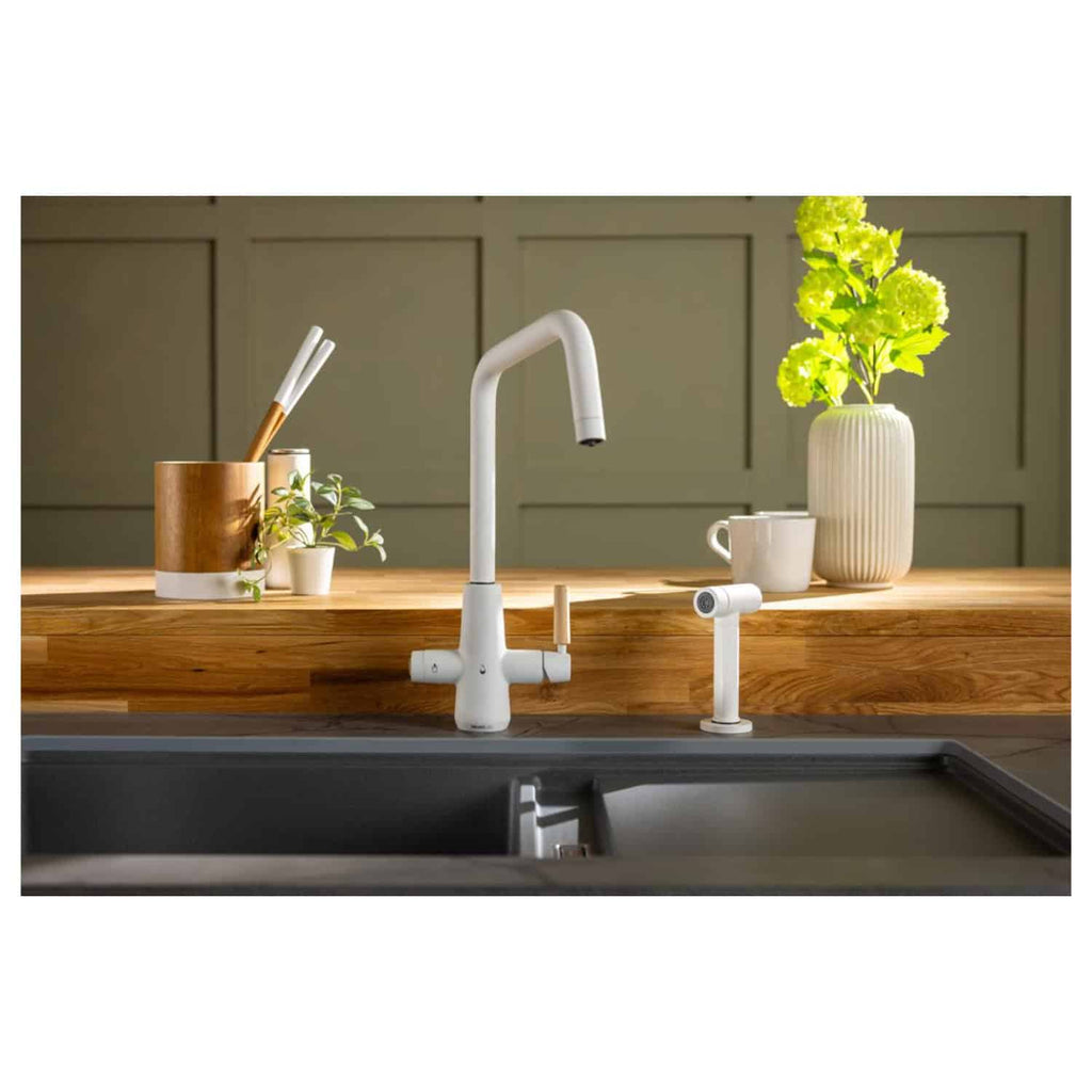 White modern kitchen sink tap with pull-out spray in a contemporary kitchen setting with wooden countertop, decorative plants, and minimalist accessories.