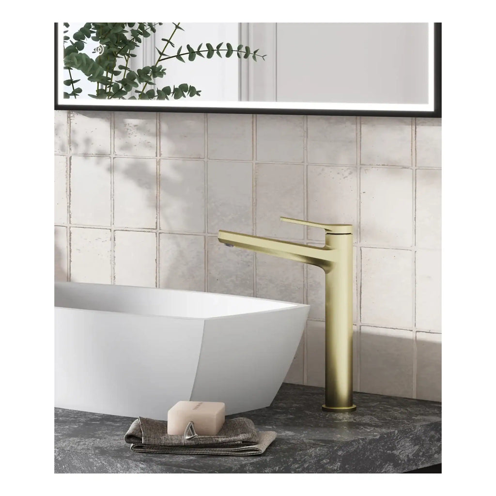 Luxurious matte gold bathroom tap next to freestanding bathtub with a modern design, set against textured beige wall tiles in a stylish contemporary bathroom.