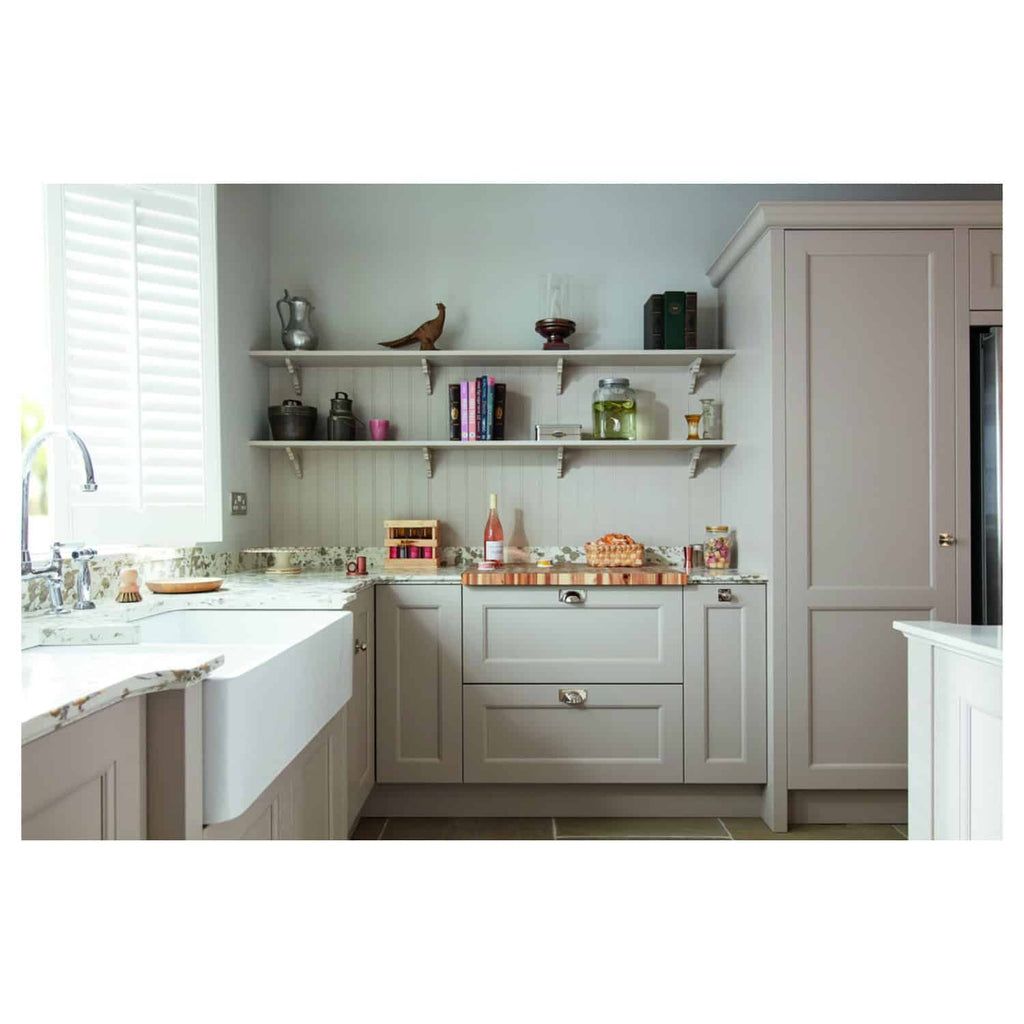 Streamlined grey kitchen cabinets with marble countertops, open shelving displaying cookbooks and decorative items, bright natural light from window with white shutters, modern and functional kitchen design.