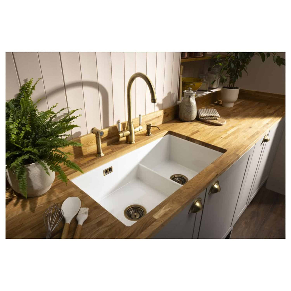 Polished brass kitchen sink tap with a farmhouse style design on a wooden worktop in a modern kitchen setting.