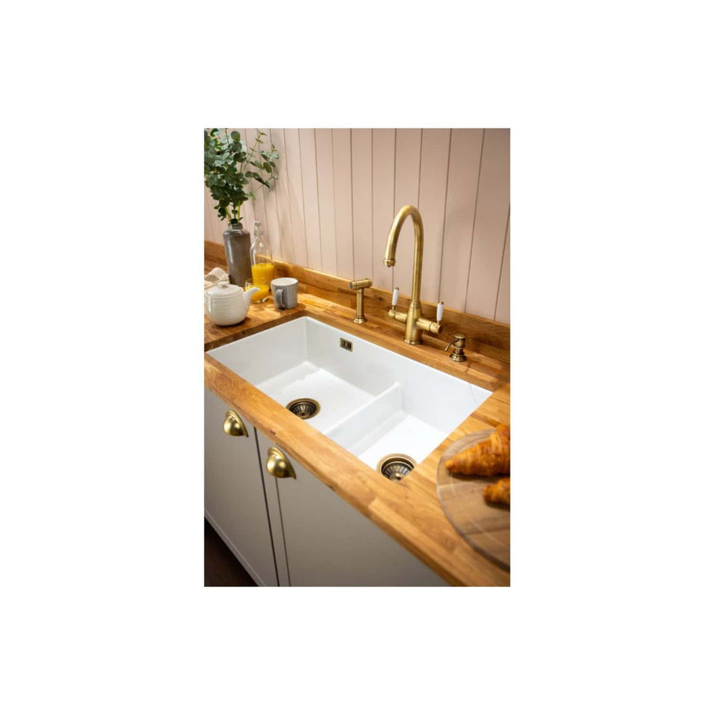 Elegant farmhouse kitchen sink with sleek brass tap and wooden countertop, complemented by fresh herbs and breakfast items, showcasing stylish and functional kitchen design.