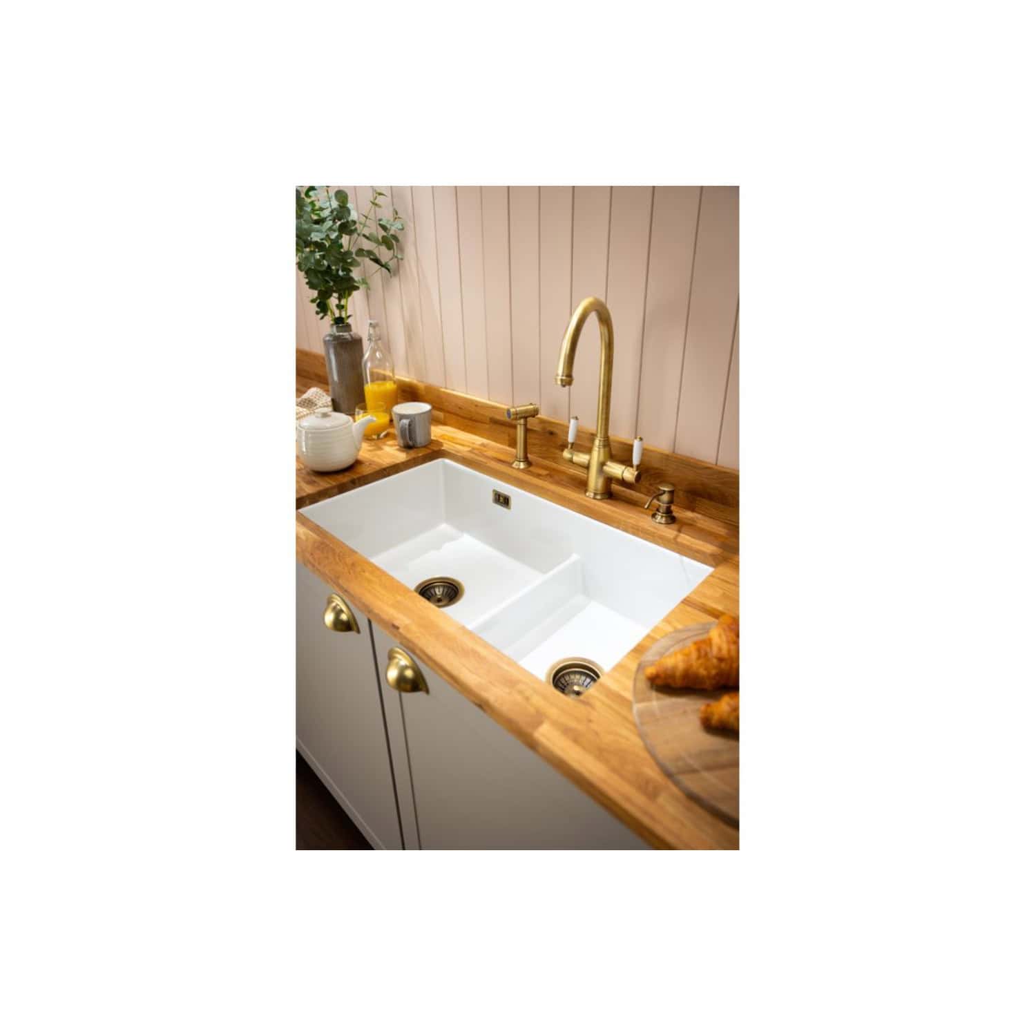 Elegant farmhouse kitchen sink with sleek brass tap and wooden countertop, complemented by fresh herbs and breakfast items, showcasing stylish and functional kitchen design.