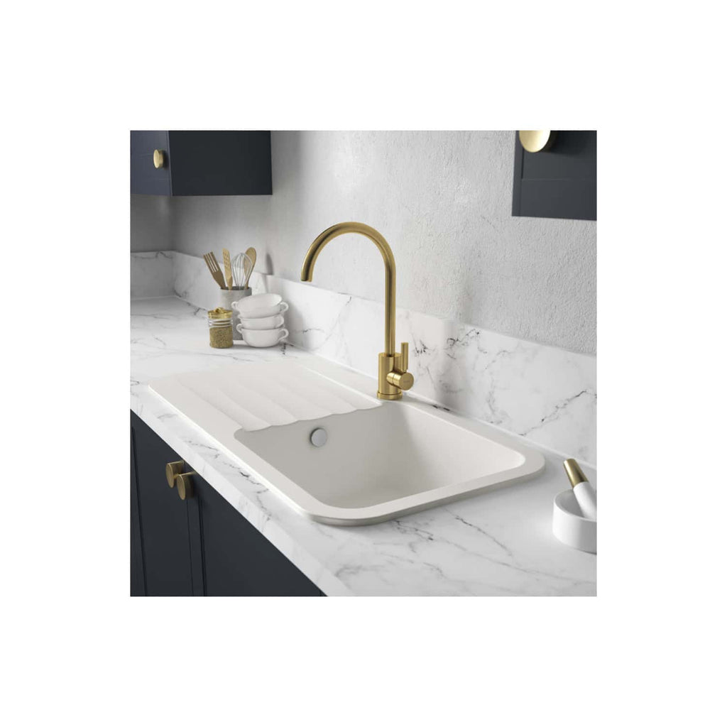 Polished gold kitchen tap with a modern high-arc design, mounted on a white marble countertop with a built-in sink, complemented by black cabinetry and kitchen accessories.