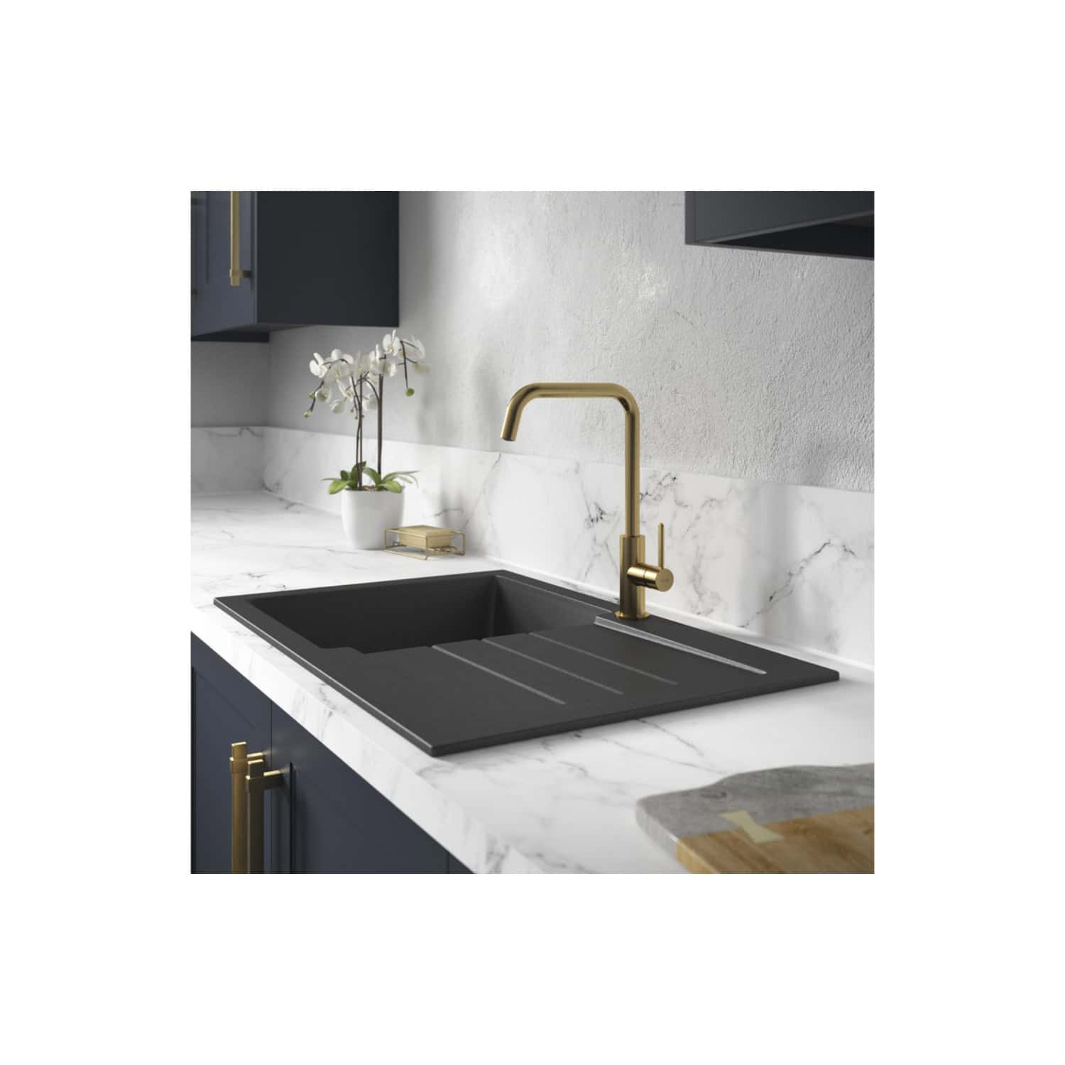 Shaker kitchen with black composite sink and brass tap in a modern bathroom or kitchen setting. Features navy blue cabinets, white marble countertops, and a decorative orchid.