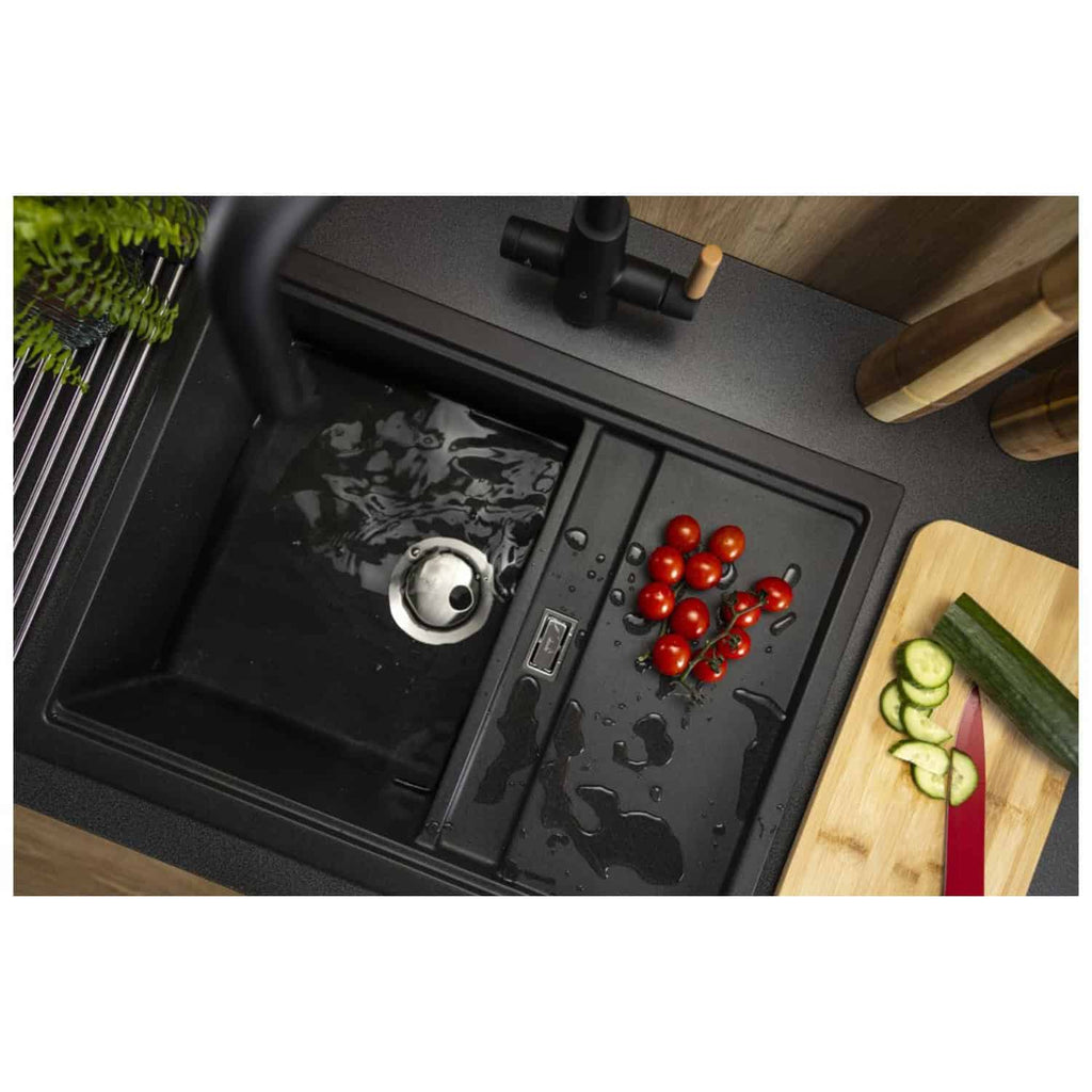 Sleek black kitchen sink with integrated drainboard, cherry tomatoes, and cucumber slices on a wooden cutting board, with modern fixtures and accessories for stylish Bubly Bathrooms.