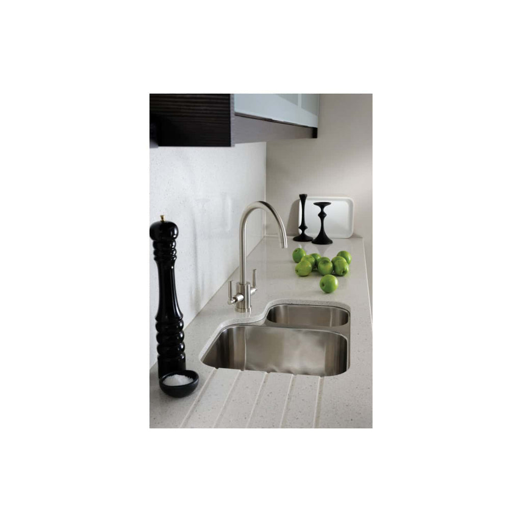 Shiny stainless steel kitchen sink with modern fixtures, black pepper grinder, green apples, and sleek black candlesticks on a light-colored countertop in a contemporary kitchen design.