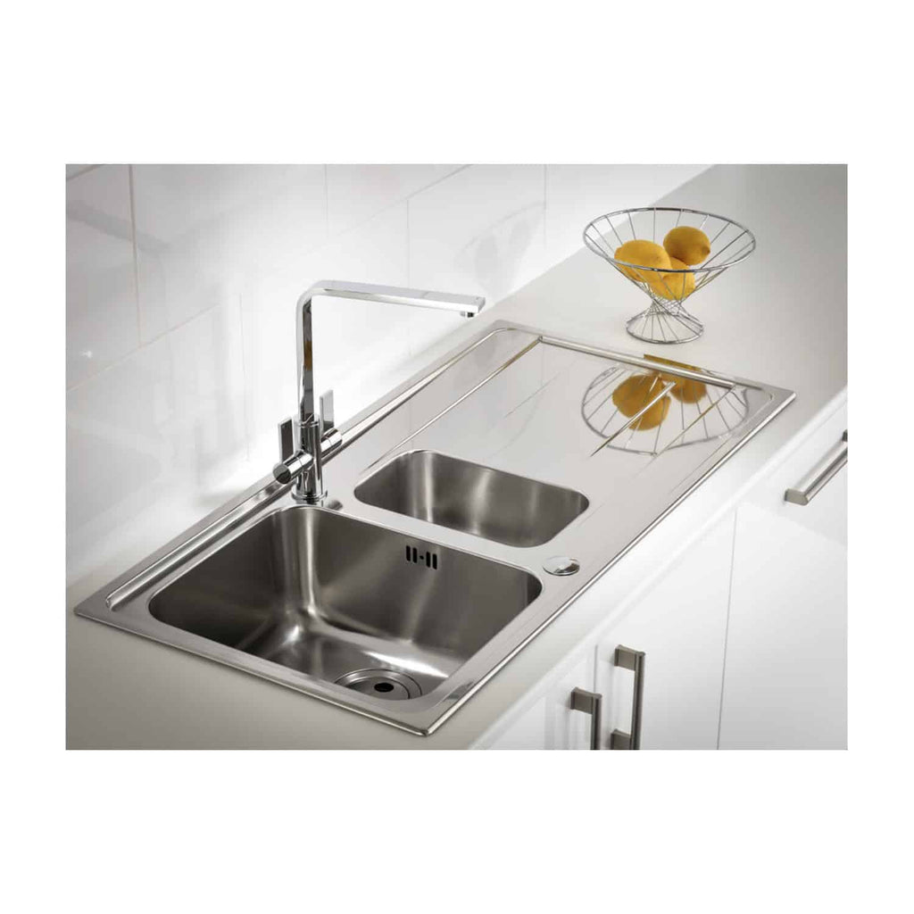Stainless steel kitchen sink with dual bowls and modern chrome tap, installed in a contemporary white kitchen with minimalist design and a wire fruit basket on the countertop.