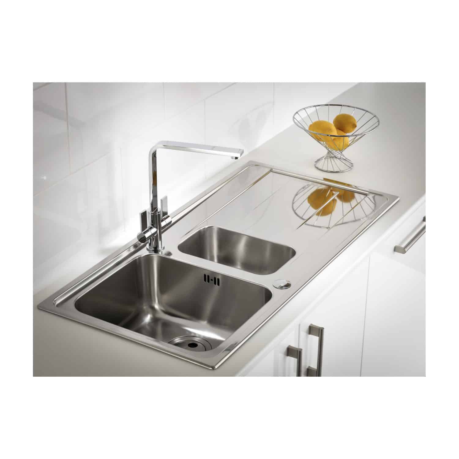 Stainless steel kitchen sink with dual bowls and modern chrome tap, installed in a contemporary white kitchen with minimalist design and a wire fruit basket on the countertop.