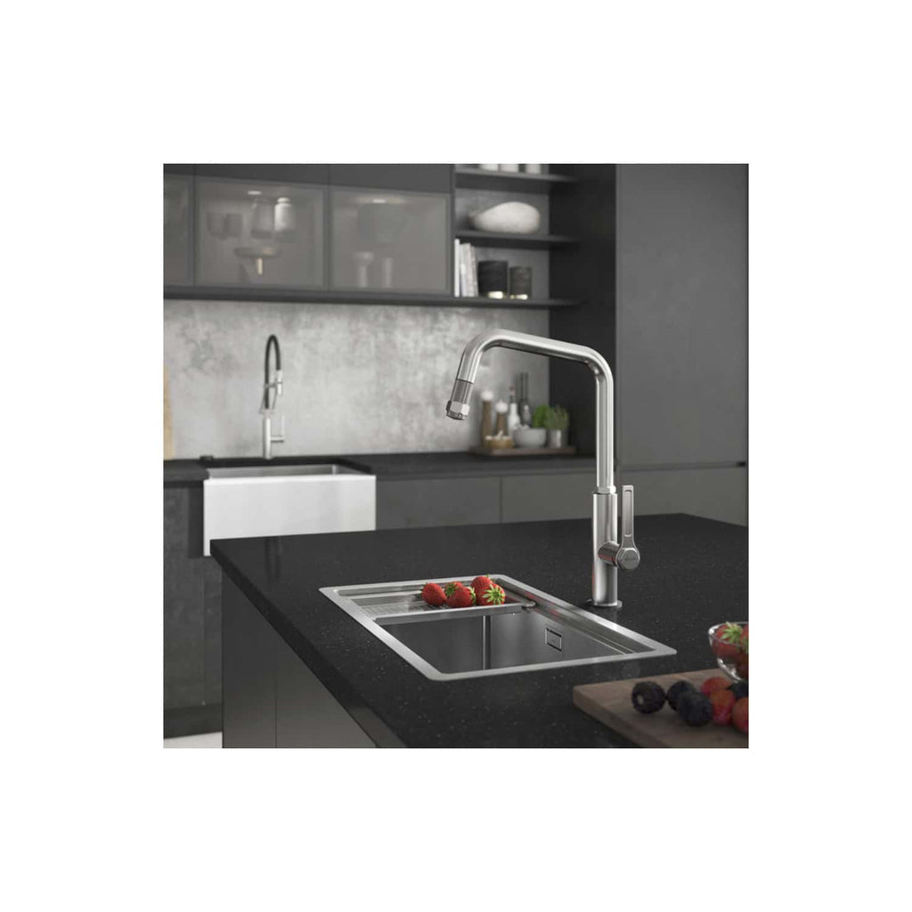 Stainless steel kitchen tap installed above a black granite sink in a modern grey kitchen with open shelving and fresh fruit.