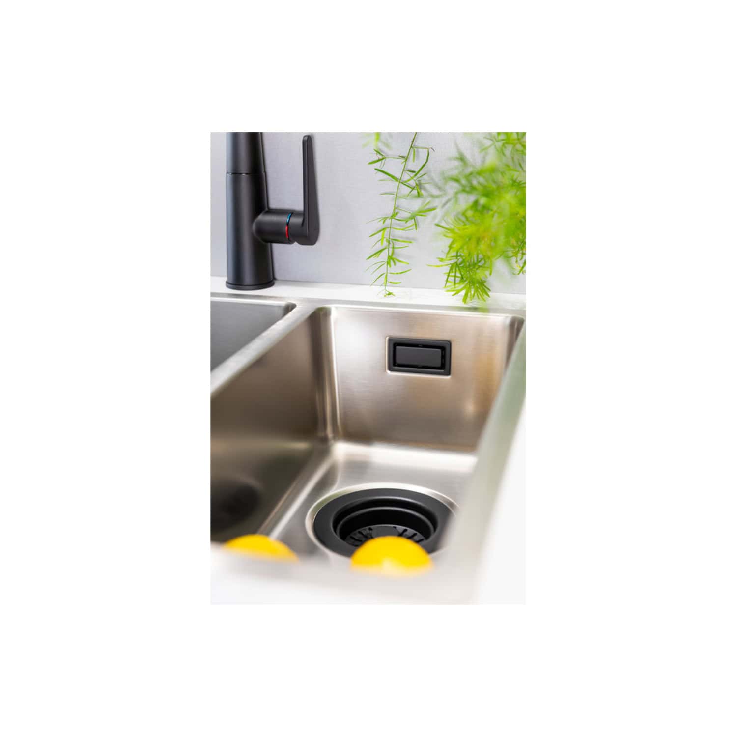 Modern stainless steel kitchen sink with black pull-down faucet and integrated soap dispenser, surrounded by green plants for a contemporary and natural look.