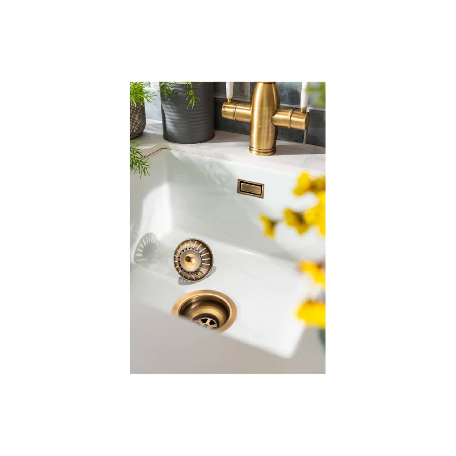 Brass kitchen sink faucet with modern design and matching drain, stylishly complemented by black plant pots and yellow flowers on the countertop, ideal for luxurious bathroom or kitchen upgrades.