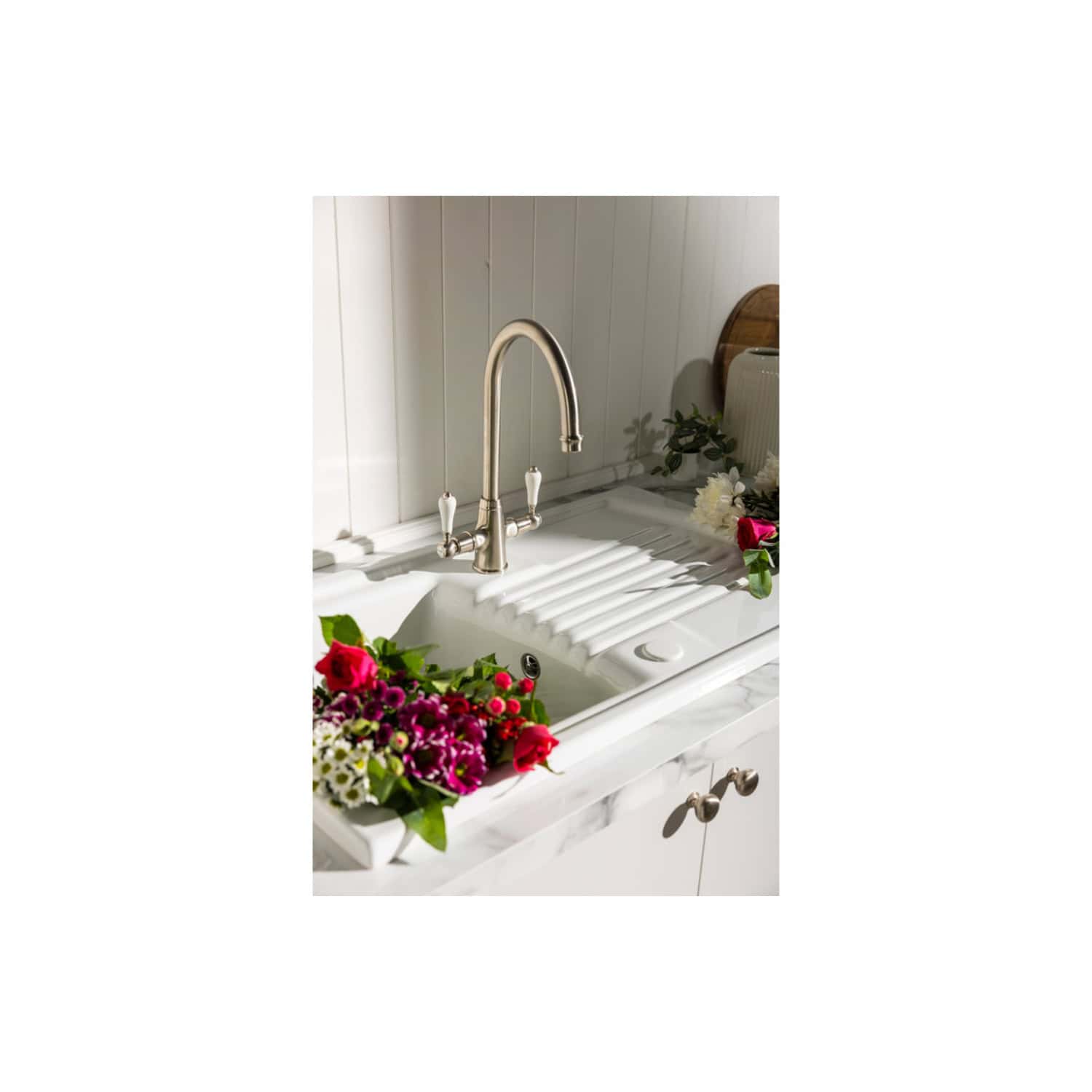 Vintage-style kitchen sink and brass tap with floral arrangements, elegant bathroom decor, and white marble countertop, perfect for sophisticated bathroom design in the UK.