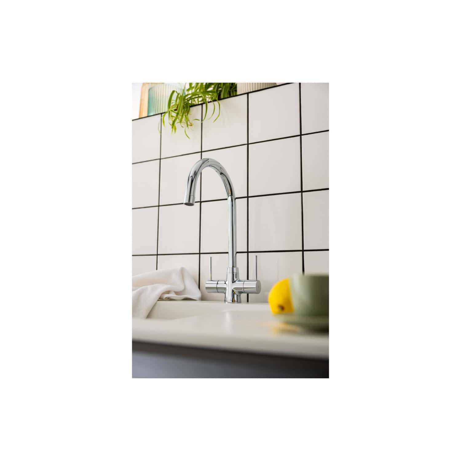 Stainless steel kitchen tap with modern curved design installed on a white sink, against a black and white tiled wall, part of Bubly Bathrooms' premium bathroom fixtures.