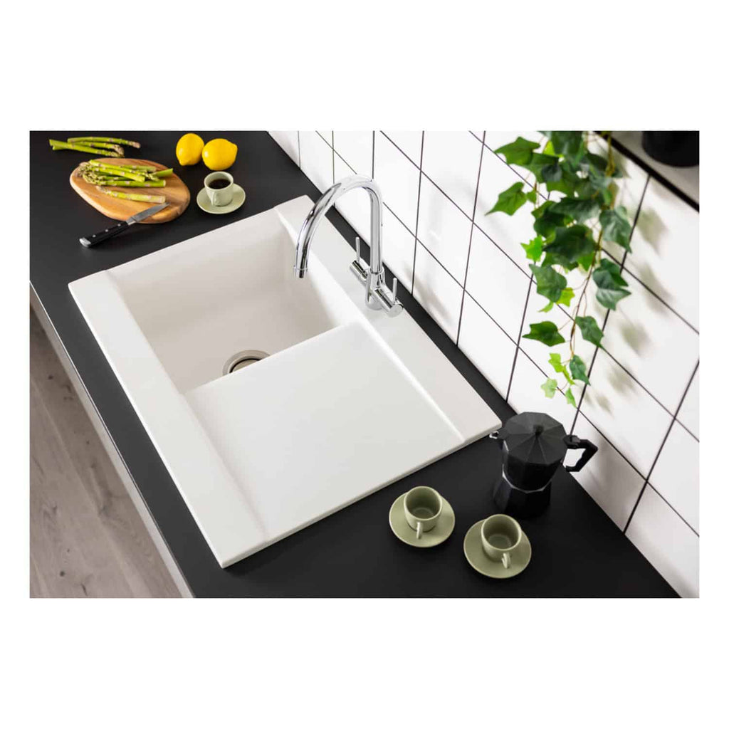 Modern white kitchen sink with integrated drainer, chrome faucet, and black countertop, complemented by fresh lemons, asparagus, coffee, and decorative greenery for stylish bathroom or kitchen design.