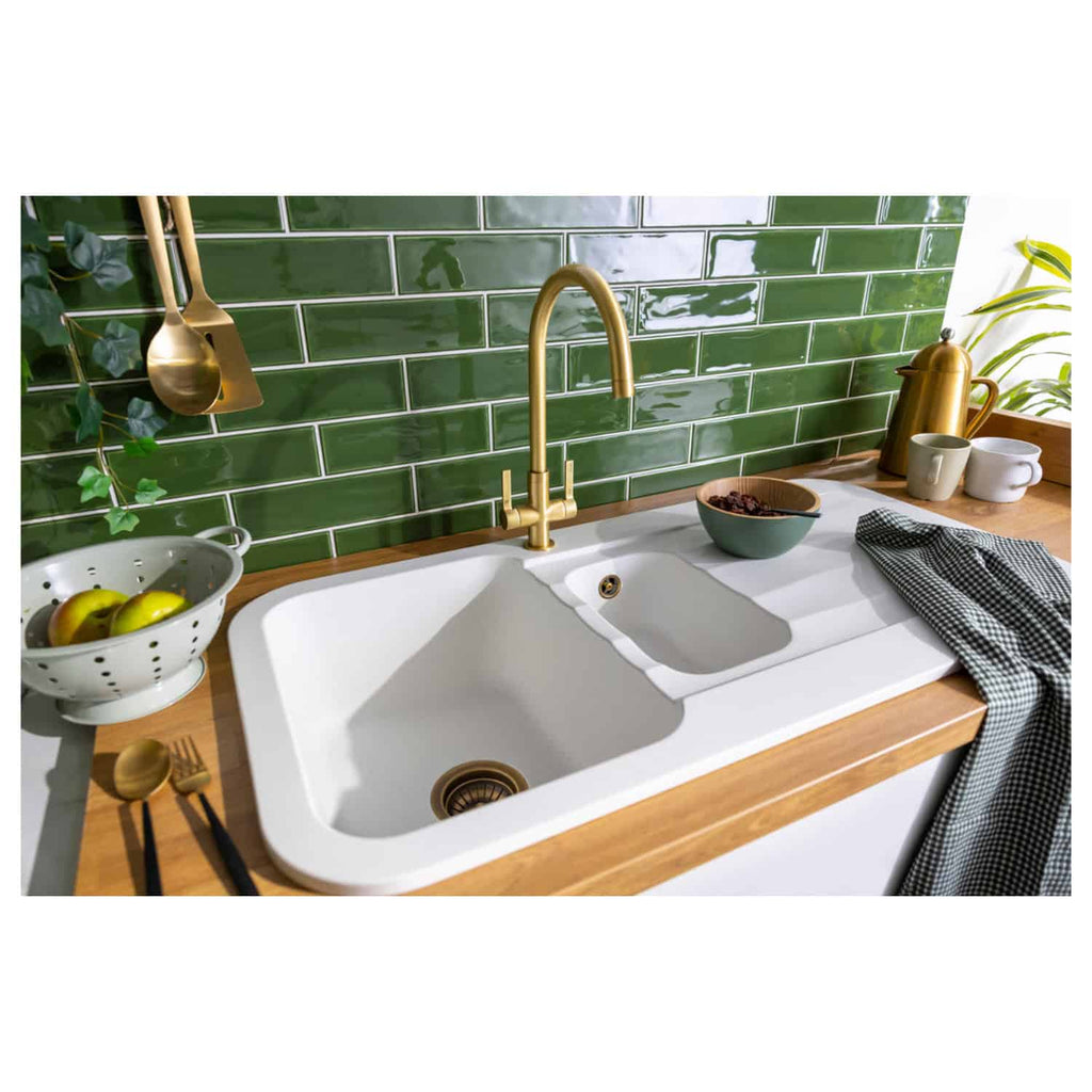Shiny white double kitchen sink with brass faucet and green tiled backsplash; stylish, functional kitchen design featuring modern appliances and decor from Bubly Bathrooms.