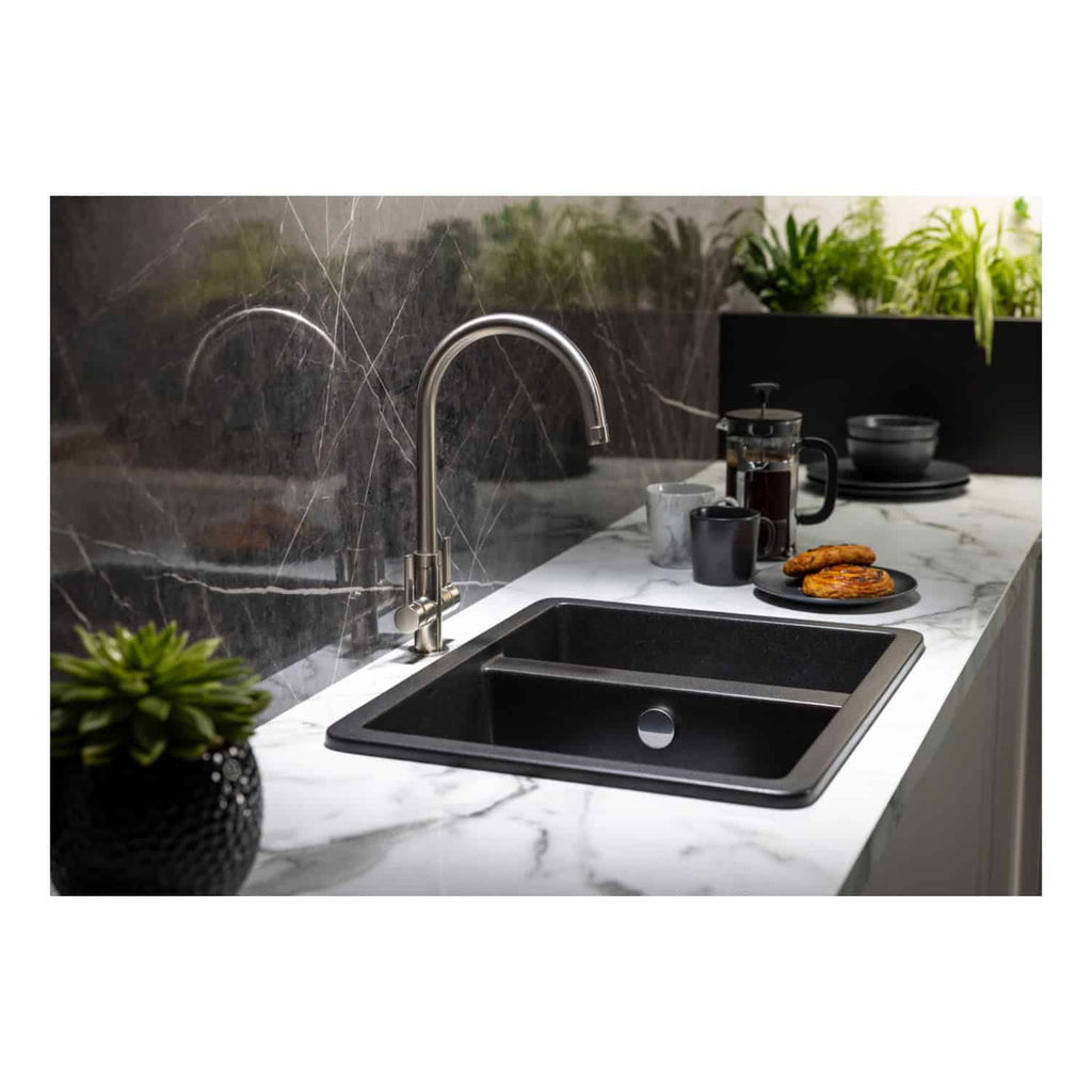Shiny stainless steel kitchen tap above a black inset sink on a marble countertop in a modern bathroom setting, featuring decorative plants and breakfast items for a stylish and functional space.