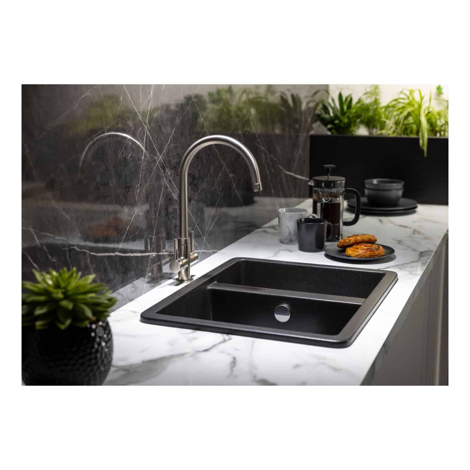 Shiny stainless steel kitchen tap above a black inset sink on a marble countertop in a modern bathroom setting, featuring decorative plants and breakfast items for a stylish and functional space.