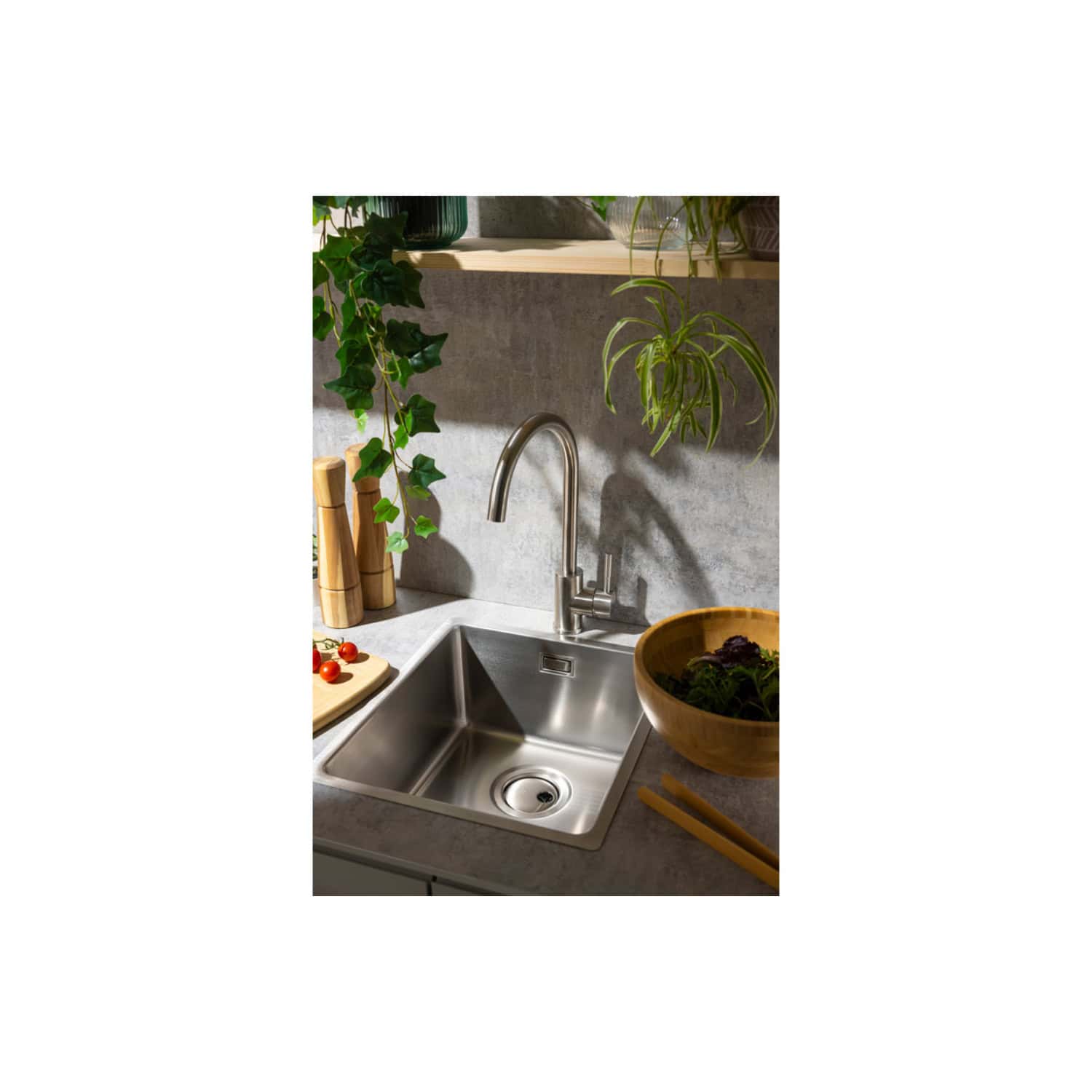Stainless steel kitchen sink with modern pull-down faucet, surrounded by greenery, wooden accessories, and fresh vegetables, showcasing elegant and functional bathroom and kitchen design.