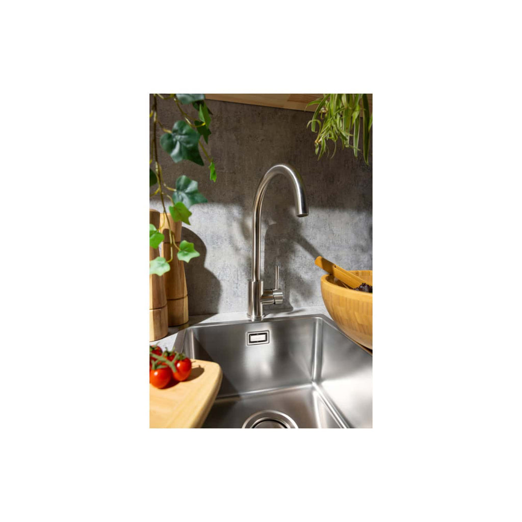 Stainless steel kitchen sink with modern faucet, surrounded by wooden utensils, fresh tomatoes, and green plants, designed by Bubly Bathrooms for contemporary kitchen decor.