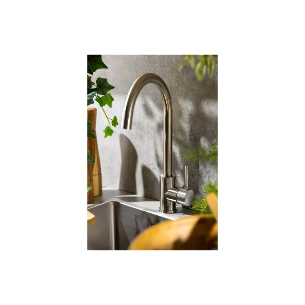 Sleek stainless steel kitchen sink faucet with modern design and high-arch spout, surrounded by greenery and natural stone backsplash, perfect for contemporary bathroom or kitchen upgrades.