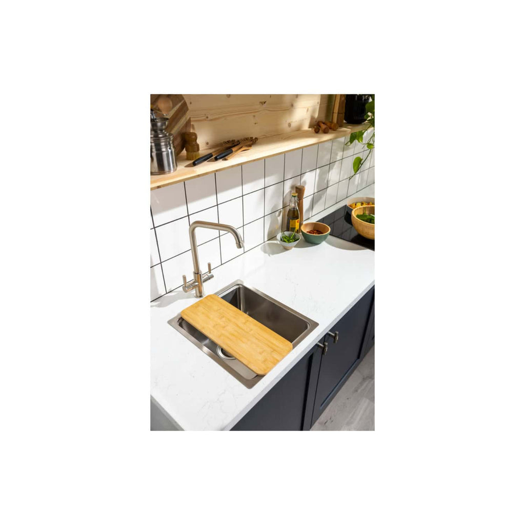 Stainless steel kitchen sink with wooden cutting board on modern white quartz countertop in contemporary kitchen. Black cabinetry, tiled backsplash, and decorative kitchen accessories enhance the kitchen design.