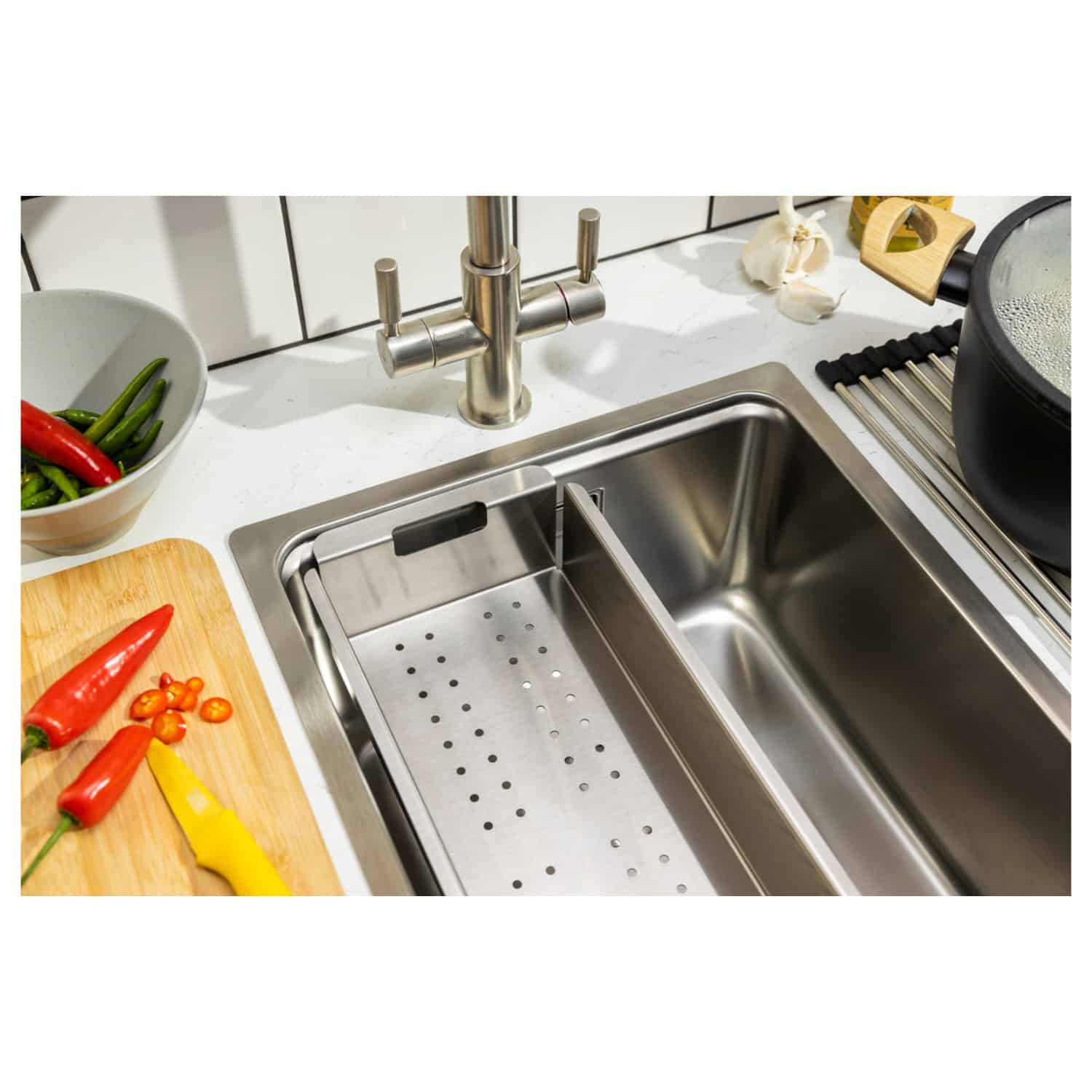 Sleek stainless steel kitchen sink with integrated draining board under modern kitchen tap, surrounded by fresh vegetables, cooking utensils, and cookware for a stylish and functional kitchen setup.