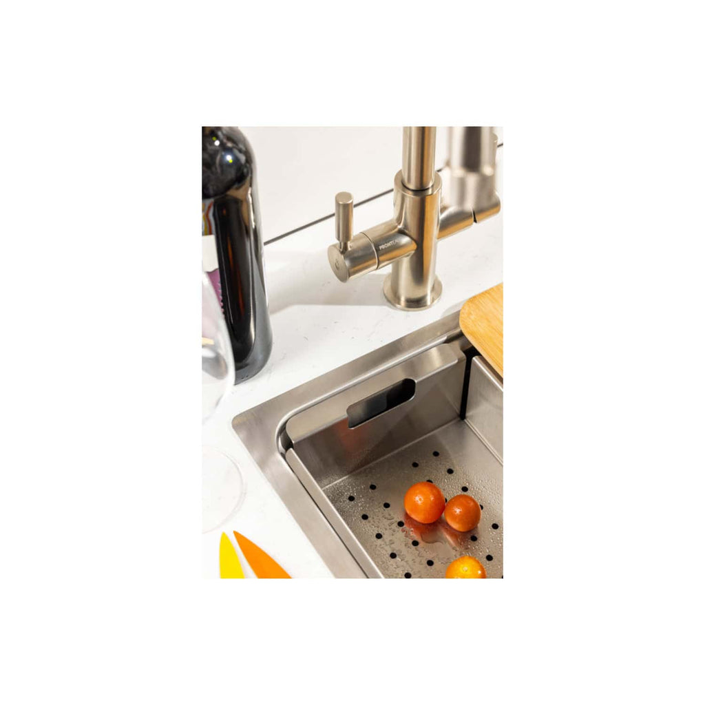 Fresh organic oranges in a stainless steel kitchen sink with a modern brushed nickel faucet, representing elegant bathroom fixtures and healthy food preparation at Bubly Bathrooms.