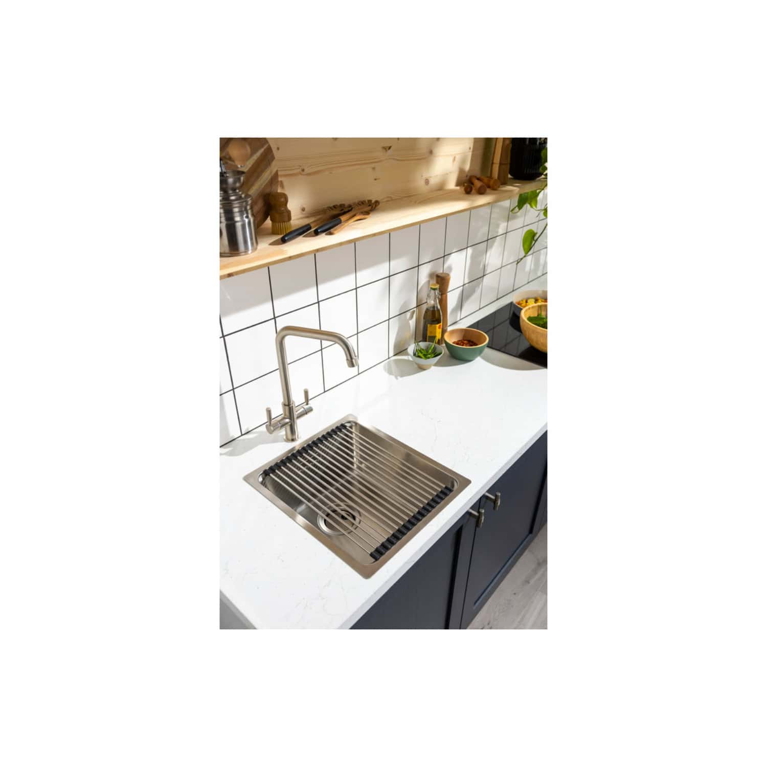 Stainless steel kitchen sink with drainer and modern mixer tap in a contemporary kitchen setting. The white worktop contrasts with dark cabinetry, surrounded by bowls and cooking ingredients.