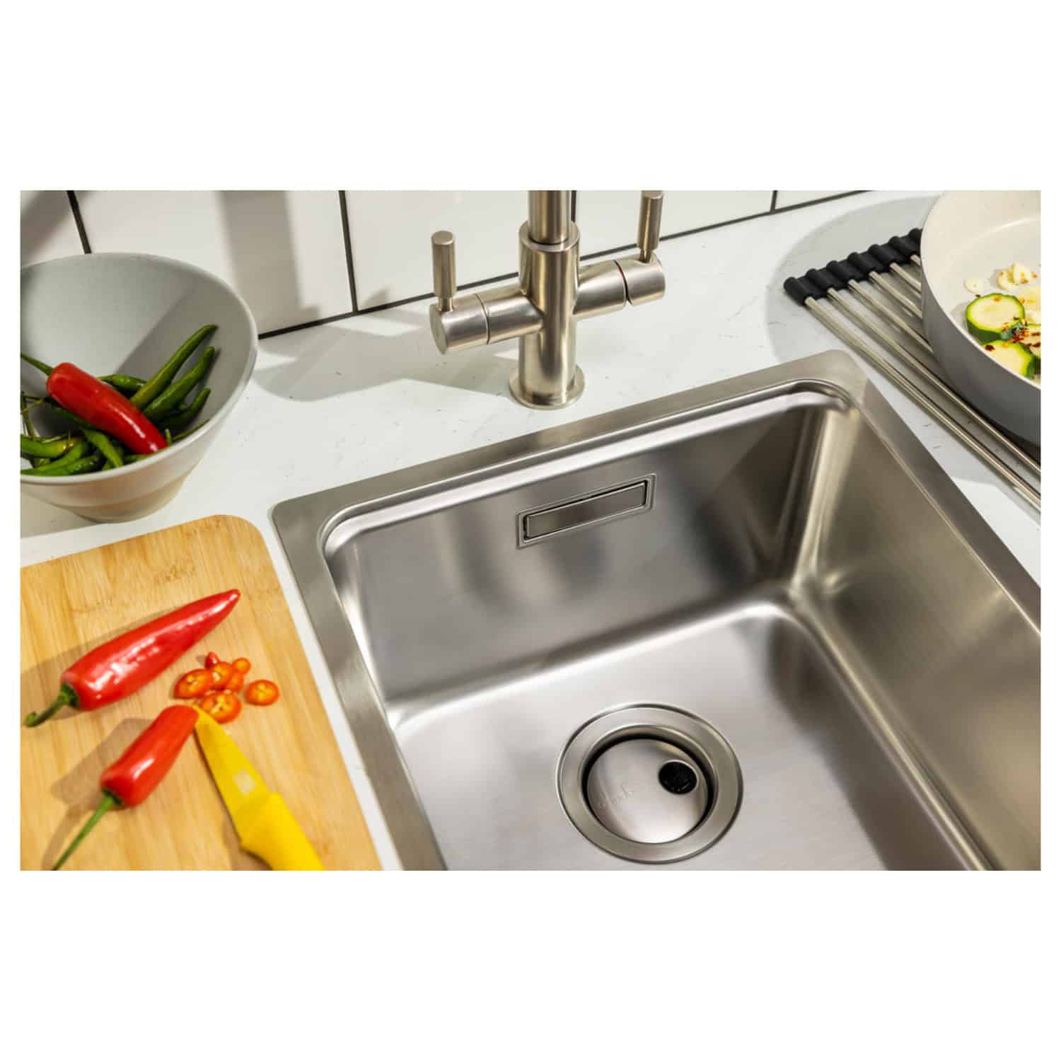 Shiny stainless steel kitchen sink with modern tap, surrounded by fresh vegetables and a wooden chopping board, perfect for cooking and meal prep in a contemporary kitchen.