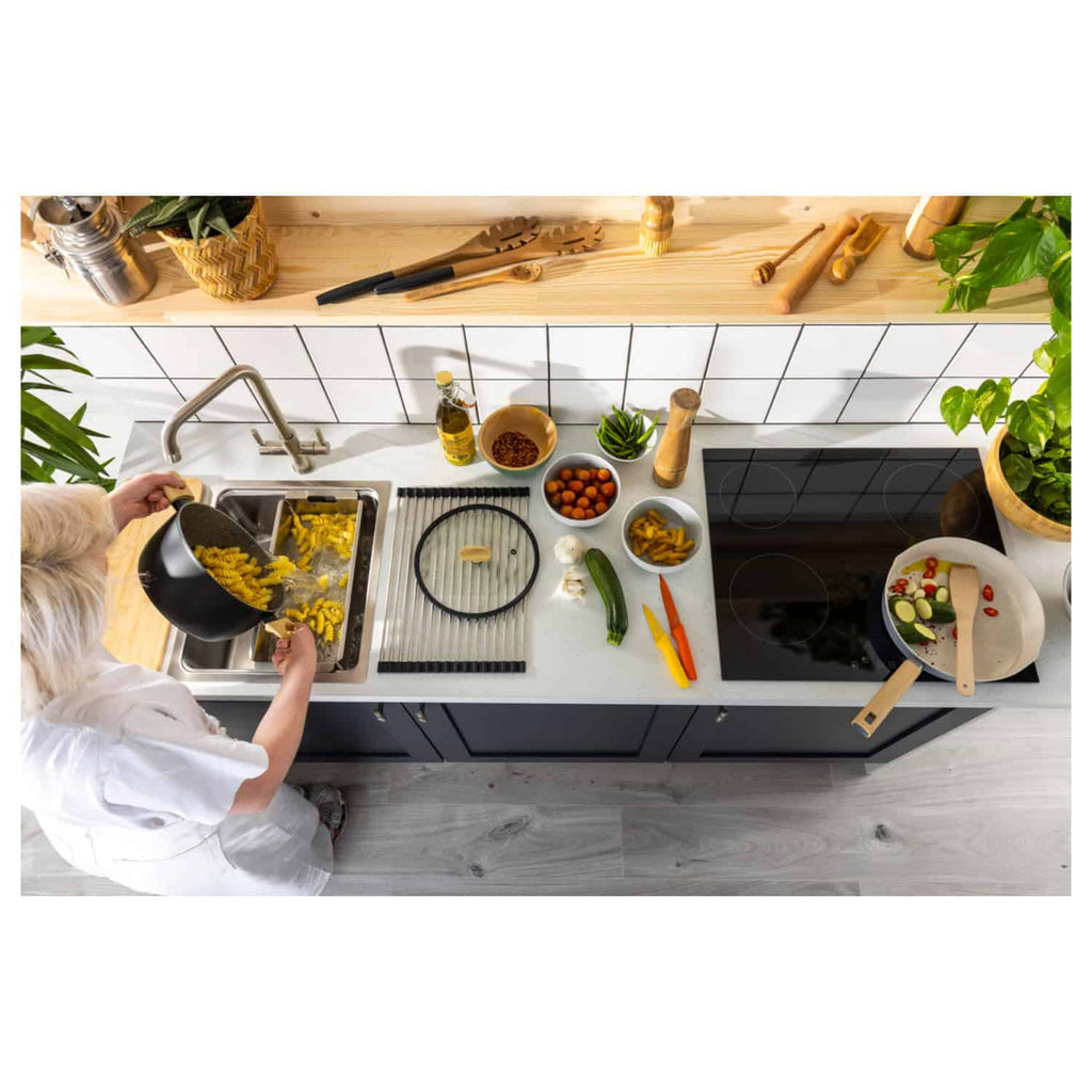 Frying yellow pasta on a modern kitchen stovetop with various fresh vegetables and cooking utensils, showcasing a stylish and functional kitchen environment.