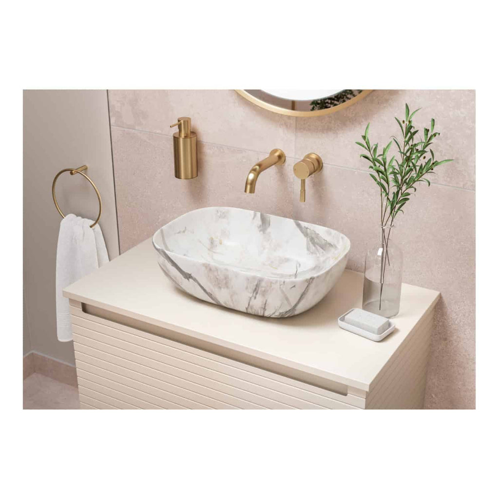 Elegant marble bathroom sink with gold fixtures, modern beige vanity, and minimalistic accessories including a vase with green branches and a soap dish. Stylish and sophisticated bathroom design.