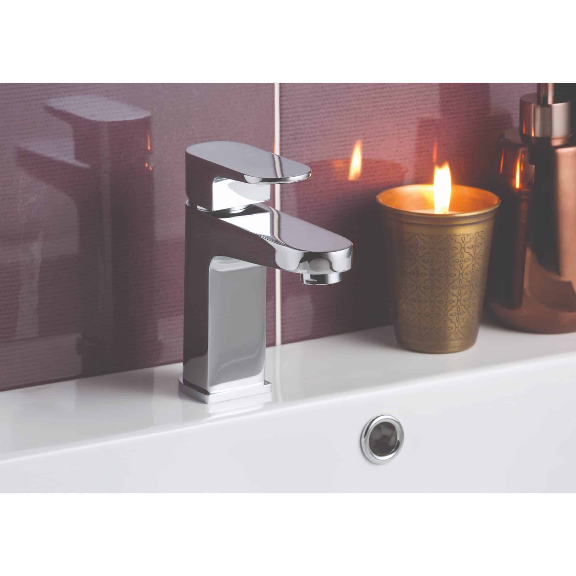 Sleek modern chrome bathroom tap on a white sink with decorative candle and minimalistic accessories in the background. Perfect for contemporary bathroom design and styling.