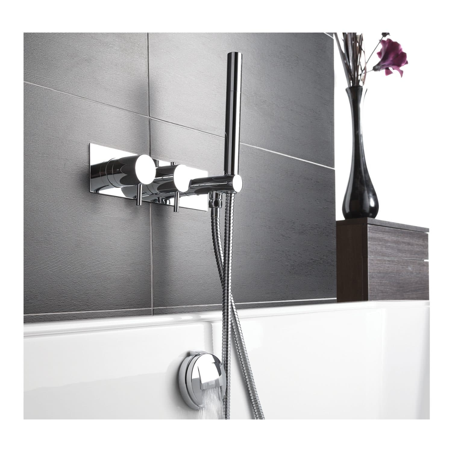 Sleek modern chrome bath tap and handheld shower faucet with a flexible hose, mounted on a textured grey bathroom wall, suited for contemporary bathroom designs.