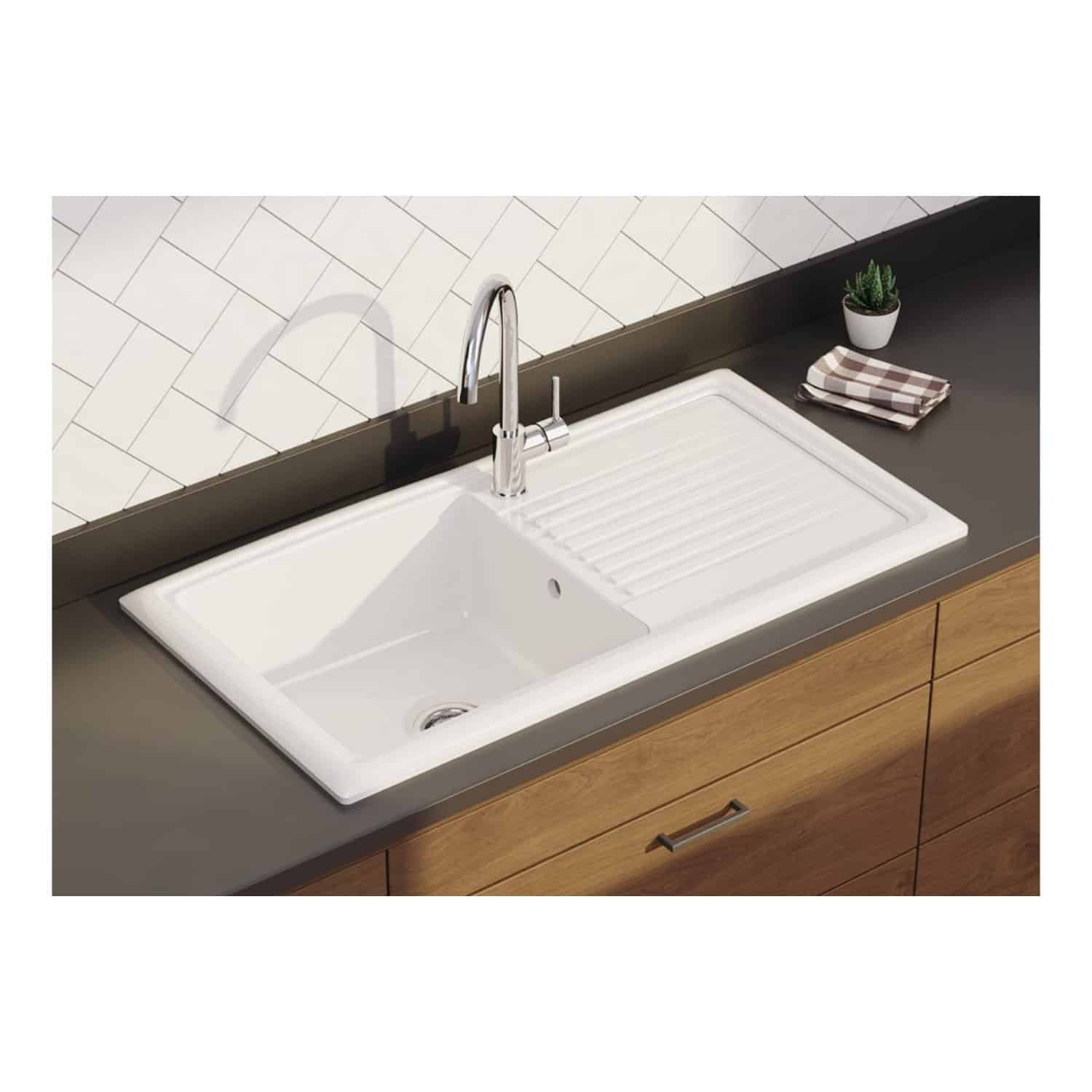 Modern white kitchen sink with built-in draining board and chrome faucet, set against a tiled backsplash with contemporary wooden cabinetry and small decorative items.