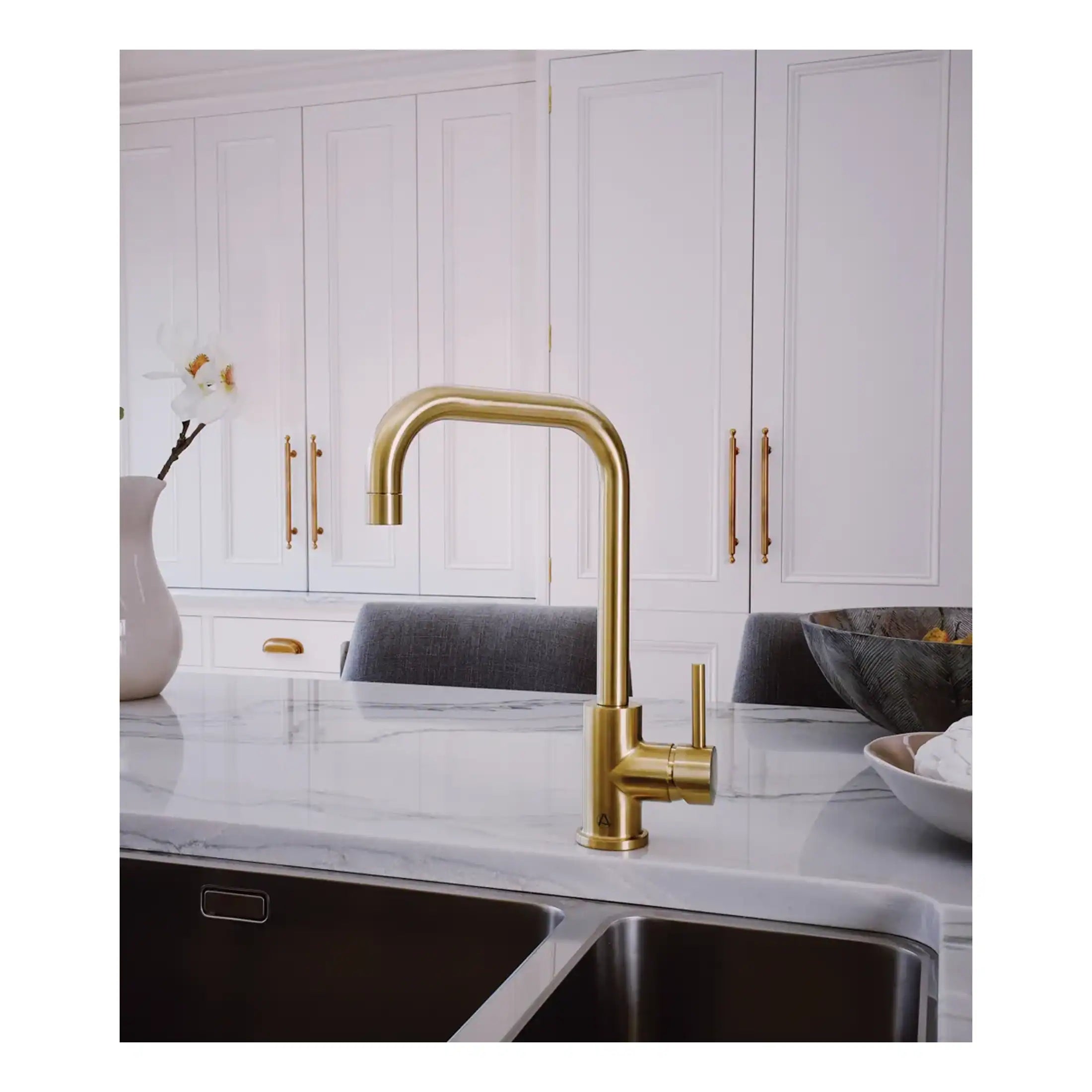 Shiny gold kitchen tap with a modern curved design, installed on a white marble countertop in a sleek, contemporary kitchen setting.