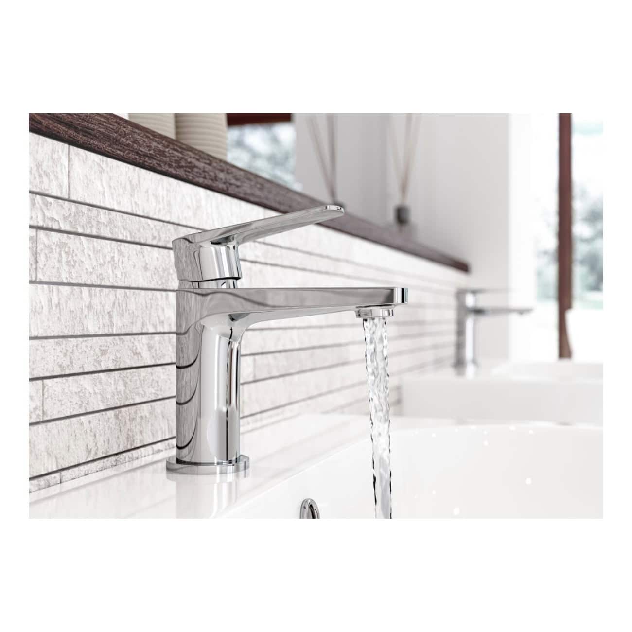 Brushed chrome bathroom mixer tap with water running over a modern white sink, reflected in natural light. Stylish, contemporary bathroom fixture surrounded by textured white tiles.