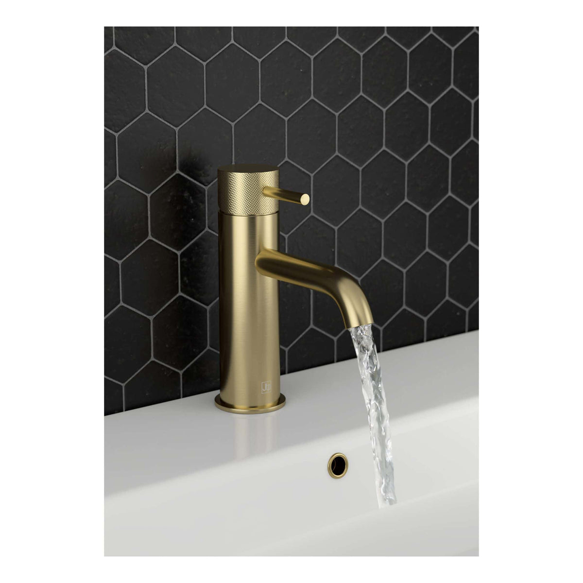 Sleek brass bathroom tap with water flowing, mounted on a white basin against a black hexagonal tiled wall, ideal for modern bathroom designs.