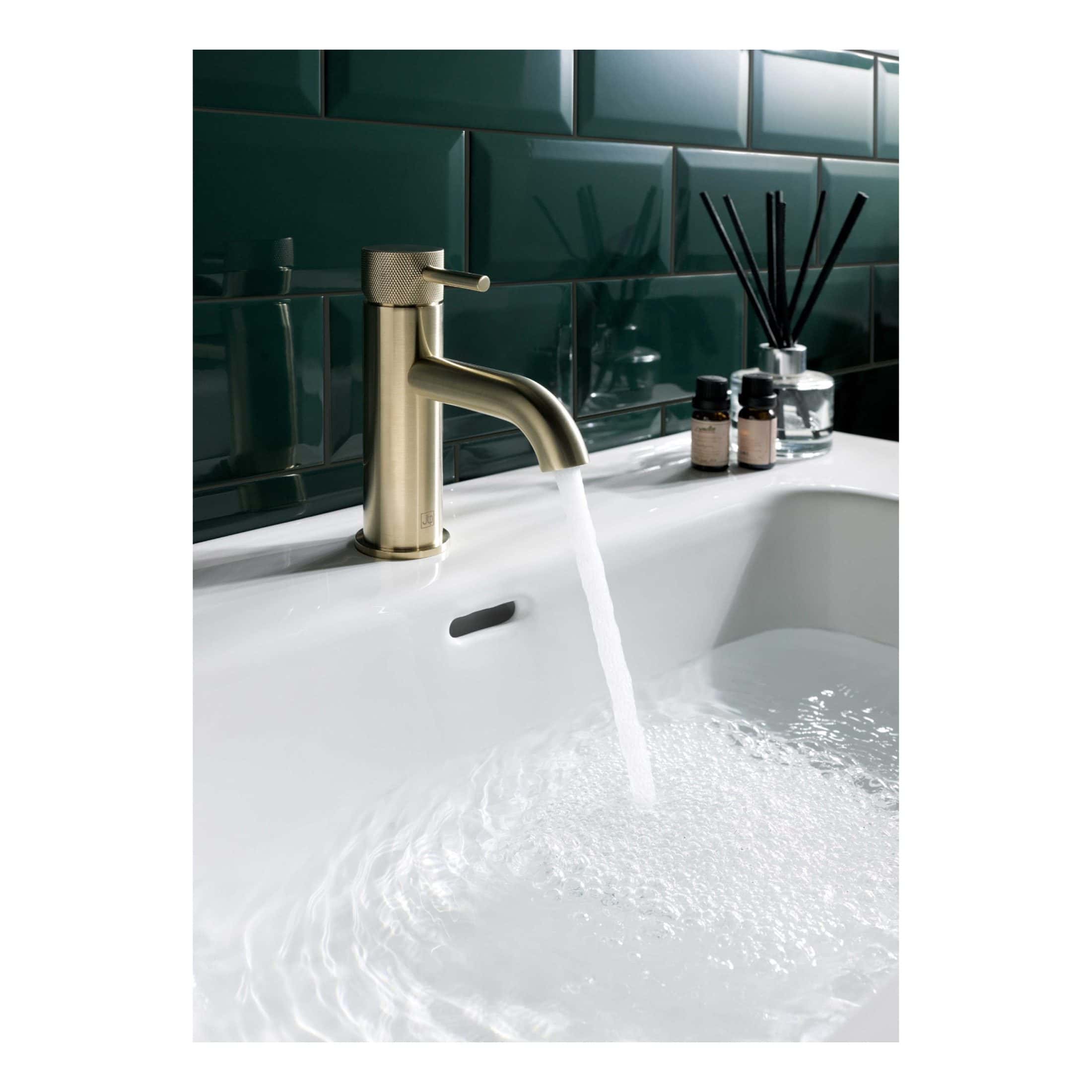 Sleek brushed gold bathroom tap with running water over a modern white sink.