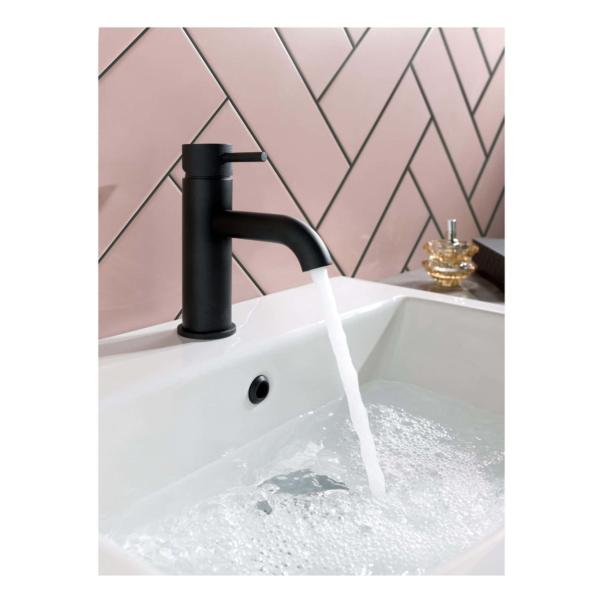 Sleek black bathroom tap with flowing water on a modern white sink, pink tiled backsplash, and decorative soap dish, showcasing contemporary bathroom fixtures and design.