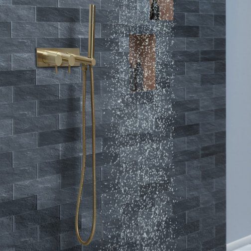 Sleek gold modern shower head with rainfall spray on dark stone tiled bathroom wall.