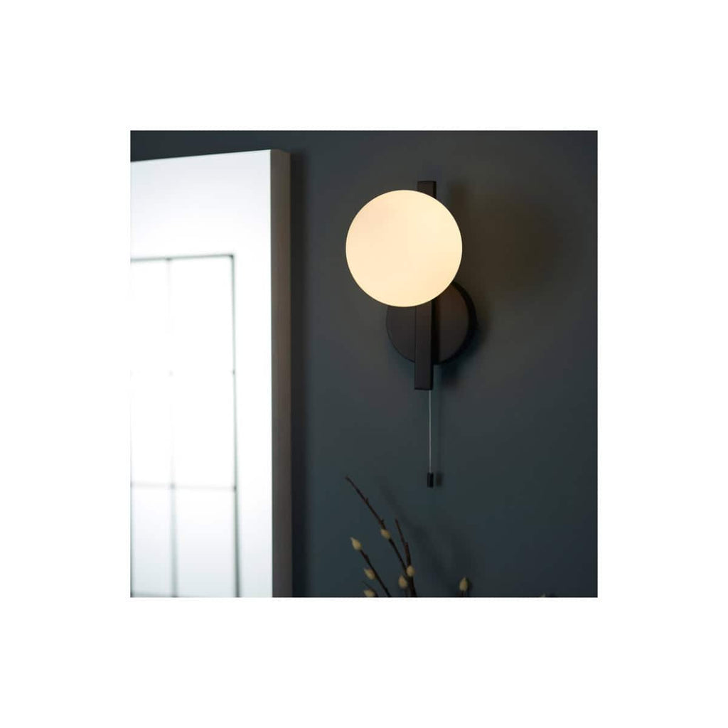 Modern wall-mounted bathroom sconce with round white globe light and black fixture, ideal for contemporary bathroom lighting.