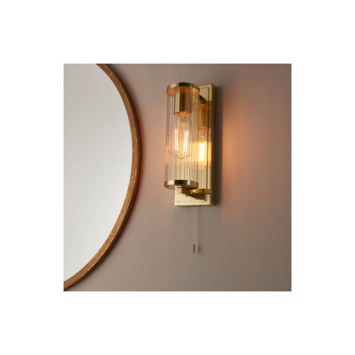 Elevated modern bathroom wall light fixture with a cylindrical glass shade and sleek brass accents, providing ambient illumination in contemporary bathroom designs.